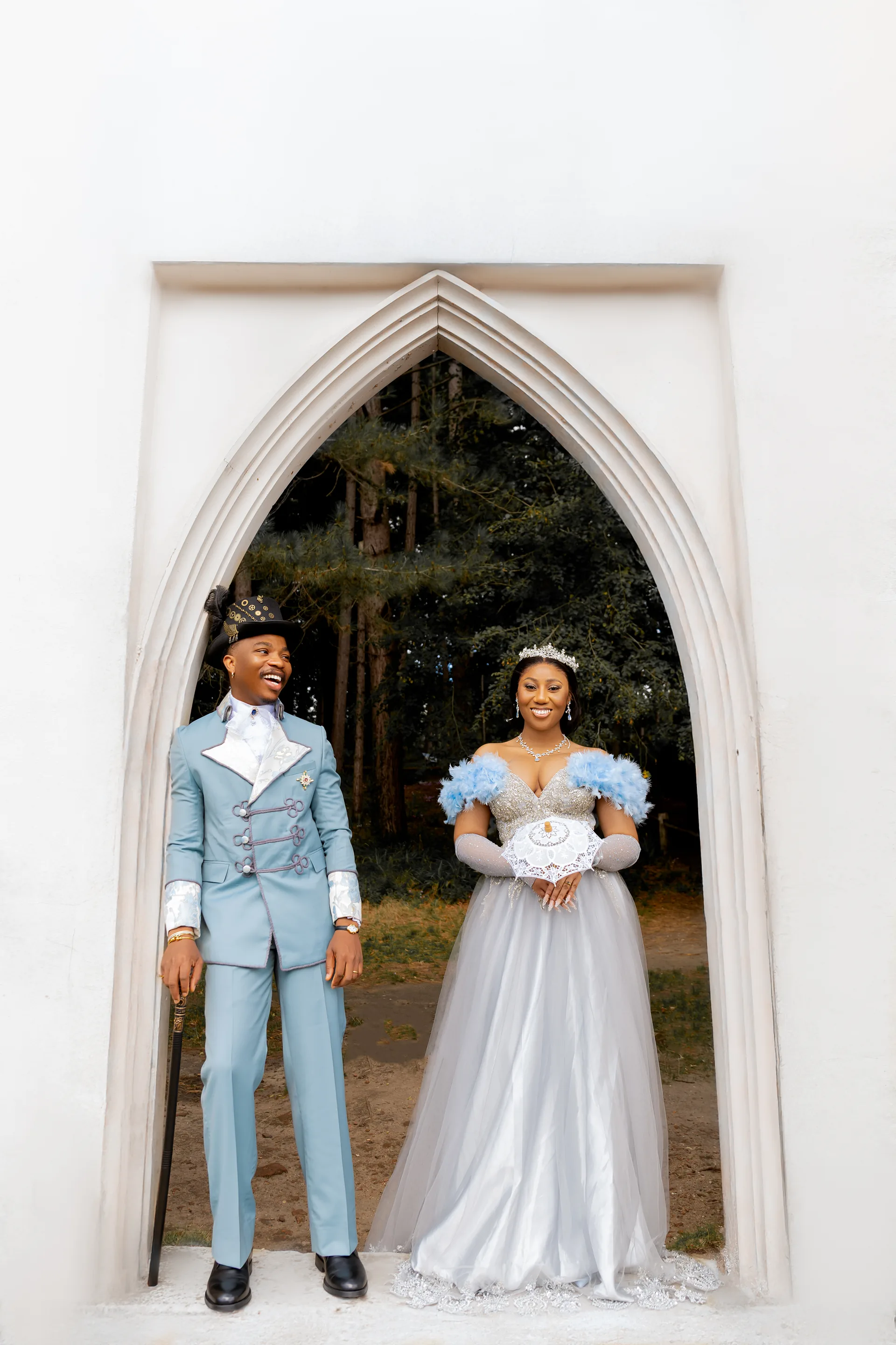 A Bride And Groom In Matching Blue Attire Looking At Each Other While Standing Inside A White Architectural Arch.